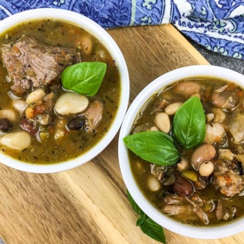 Two white bowls full of 15 bean soup topped with basil.