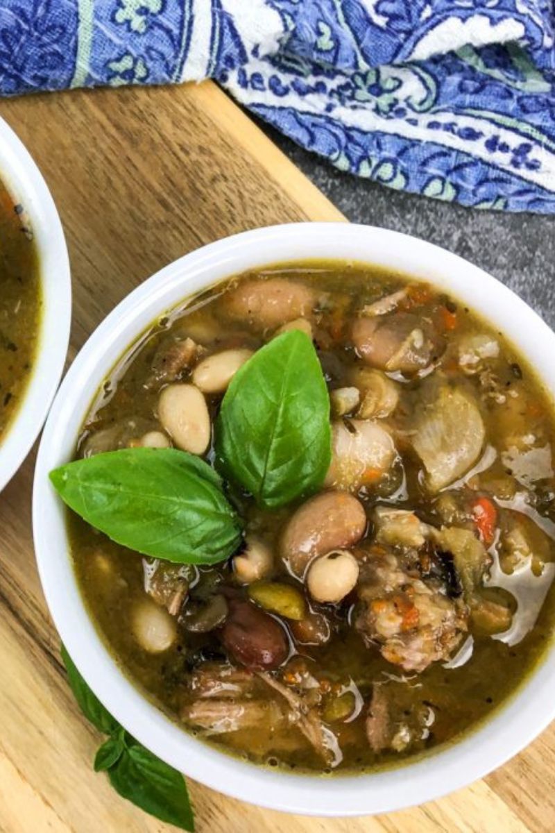 Two white bowls full of 15 bean soup topped with basil. 